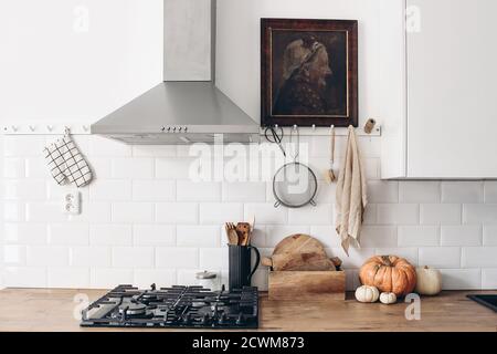 Cuisine moderne éclectique avec citrouilles. Mur de briques blanches avec carreaux de métro, rails de suspension et peinture à l'huile. Comptoir en bois, hotte et cuisinière à gaz Banque D'Images