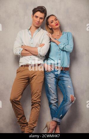 couple debout posant en arrière-plan studio, homme avec les mains croisées tandis que la femme avec la main dans la poche touche l'épaule de l'homme Banque D'Images