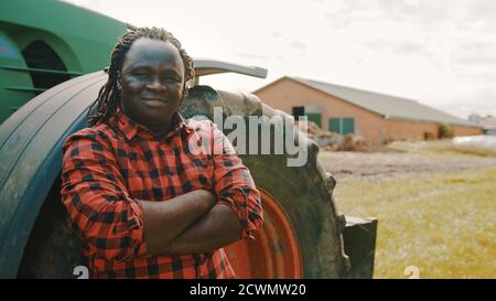 Un jeune agriculteur africain qui s'appuie sur le pneu du tracteur. Photo de haute qualité Banque D'Images
