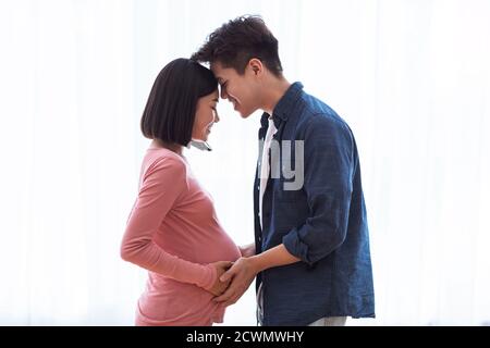 Le mari asiatique touchant le ventre de la femme enceinte près de la fenêtre à l'intérieur Banque D'Images