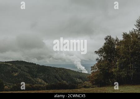 Vers le ciel, la vapeur s'élève des tours de refroidissement de puissance Plante se cachant dans la vallée des montagnes Ore en République tchèque pendant la journée d'automne nuageux Banque D'Images
