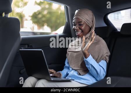 Réunion d'affaires en ligne. Femme d'affaires musulmane effectuant des appels vidéo avec un ordinateur portable en voiture Banque D'Images