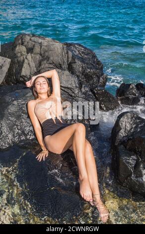 Femme caucasienne bain de soleil se relaxant sur une plage côtière rocheuse. Pieds détendus dans la mer d'eau à Los Roques Venezuela Banque D'Images