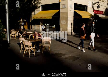 Dans le centre-ville de Barcelone, les personnes portant des masques pour empêcher la propagation du coronavirus marchent devant une terrasse de bar. Banque D'Images