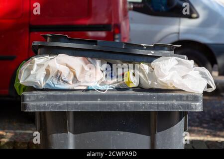 Une poubelle à roulettes dans la rue débordant de déchets Banque D'Images