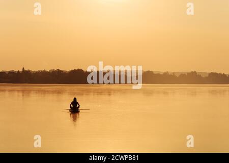 Homme sportif assis sur un paddle board au milieu de la brumeuse lac Banque D'Images