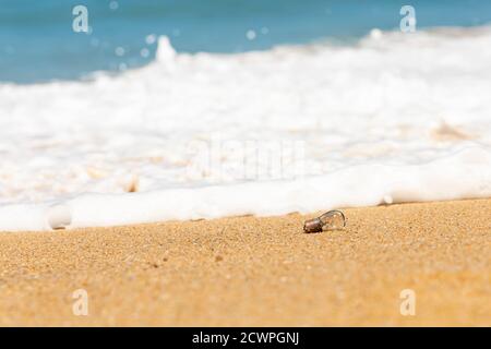 Une vieille ampoule repose sur la plage de sable et les vagues de mer. Banque D'Images