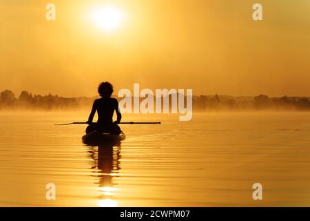 Homme assis à paddle-board et profitant d'un lever de soleil incroyable Banque D'Images