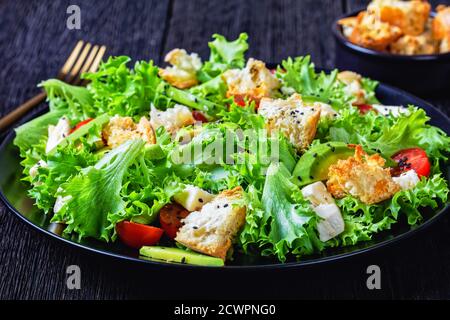 salade de feuilles avec avocat, tomates cerises, mozzarella et croûtons parsemés de graines de sésame noir sur une assiette, sur une table en bois, vue sur le paysage Banque D'Images