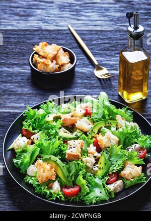 salade feuillue avec avocat, tomates cerises, mozzarella et croûtons parsemés de graines de sésame noir sur une assiette, sur une table en bois, vue verticale depuis Banque D'Images