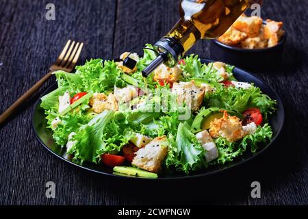 gros plan de salade feuillue avec avocat, tomates cerises, mozzarella et croûtons parsemés de graines de sésame noir sur une assiette, sur une table en bois, landsc Banque D'Images