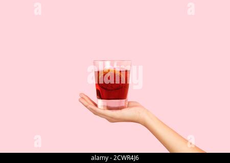 Femme main tenant un verre de vermouth rouge sur un fond rose Banque D'Images