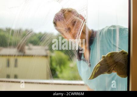 Un homme d'âge moyen qui nettoie la fenêtre avec un chiffon et un nettoyant pour vitres Banque D'Images