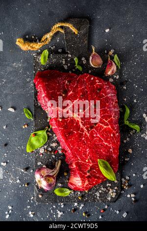 Steak de bœuf cru sur fond noir, avec herbes et épices, vue du dessus. Banque D'Images