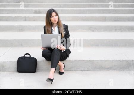 Jeune femme d'affaires utilisant un ordinateur portable dans la ville, assise sur un escalier. Photo de haute qualité Banque D'Images