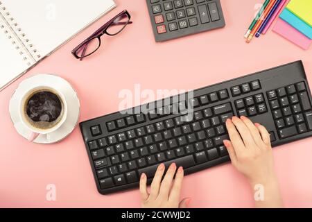 Espace de travail Flat Lay. Femme travaillant sur pc, tasse de café, calculatrice, ordinateur, ordinateur portable, planificateur et stationnaire avec espace de copie sur fond de table rose. Banque D'Images