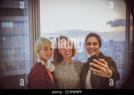 Femmes d'affaires souriantes emportant le selfie à la fenêtre du bureau Banque D'Images