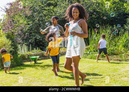 Bonne famille jouant et bulles soufflantes dans le jardin d'été ensoleillé Banque D'Images