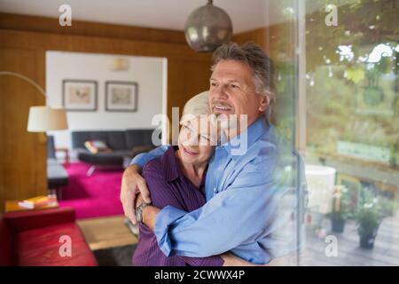 Un couple de personnes âgées heureux se hante devant la fenêtre ensoleillée du salon Banque D'Images