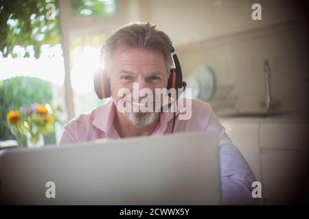 Portrait souriant homme senior avec casque travaillant sur ordinateur portable Banque D'Images