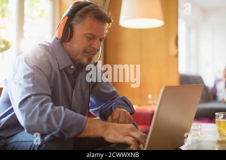Homme âgé avec casque utilisant un ordinateur portable sur le canapé du salon Banque D'Images