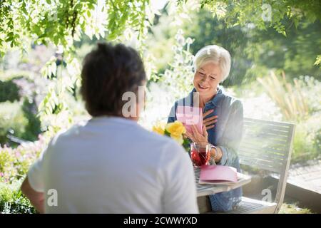Bonne femme senior cadeau d'ouverture de mari pendant l'été ensoleillé patio Banque D'Images