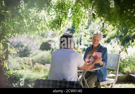 Une femme âgée heureuse ouvre un cadeau de son mari sur le patio d'été Banque D'Images