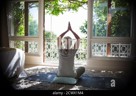 Femme sénior pratiquant le yoga à la porte ensoleillée et tranquille du balcon Banque D'Images