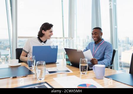 Hommes d'affaires souriants travaillant sur des ordinateurs portables dans une salle de conférence en hauteur Banque D'Images