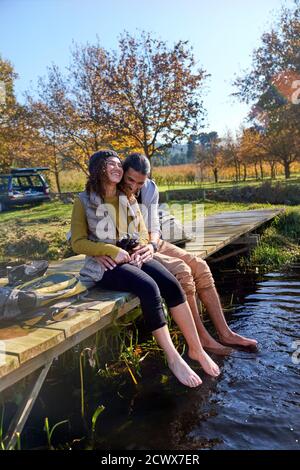 Un jeune couple affectueux, pieds nus, rit sur un quai ensoleillé Banque D'Images