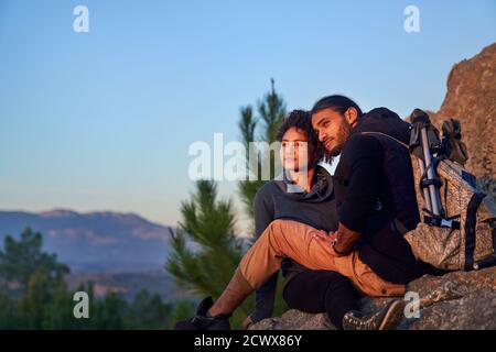 Jeune couple de randonnée serein profitant du coucher de soleil sur les rochers Banque D'Images