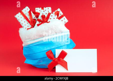 Sac de Noël du Père Noël avec cadeaux dans un masque protecteur sur fond rouge avec note maquette. Le concept de vacances pendant le coronavir Banque D'Images