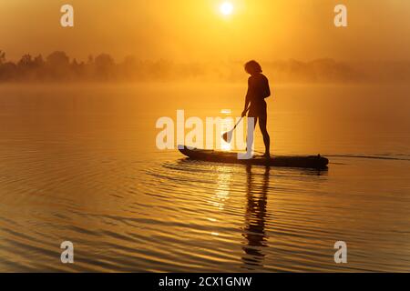 Silhouette d'homme sportif pagayant à bord sur un lac brumeux Banque D'Images