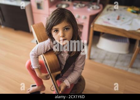 Jeune fille avec des yeux brun foncé sur un tabouret tenant petit guitare Banque D'Images