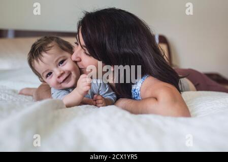Une mère aimante embrasse un bébé souriant tout en étant allongé lit Banque D'Images