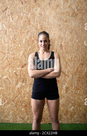 Portrait d'une belle jeune femme sportive avec les bras croisés debout contre le mur de liège à la salle de gym Banque D'Images