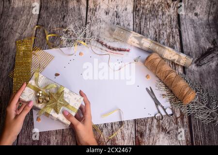Mise en page de Noël. Pose à plat... Les mains de la fille tiennent un cadeau du nouvel an sur un fond en bois. Banque D'Images
