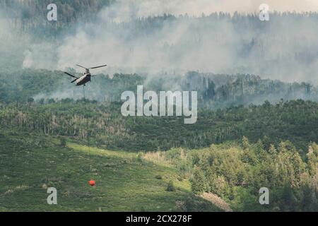 Hélicoptère volant avec un produit ignifuge alors que de la fumée s'échappe d'un feu de forêt en forêt Banque D'Images