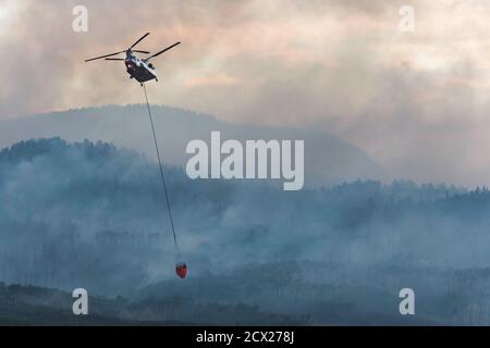 Hélicoptère militaire volant avec un produit ignifuge alors qu'il émet de la fumée feu de forêt au coucher du soleil Banque D'Images