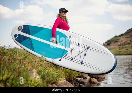 Femme souriante avec paddleboard au bord du lac contre le ciel Banque D'Images