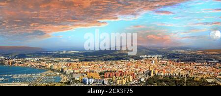 Vue panoramique en grand angle depuis le sommet du rocher de Gibraltar surplombant Malaga, avec des nuages orangés et la lune surplombant Malaga Banque D'Images