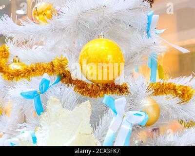 Boules d'or et noeuds de tinsel et blanc-bleu sur les branches D'un arbre de Noël blanc Banque D'Images