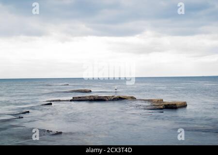 Plan de longue exposition de roches sortant de l'eau et du ciel adramatique, de vagues calmes et de formations rocheuses vives, vue magnifique sur l'océan et le ciel à Kimmeridge Banque D'Images