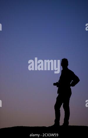 Figure solitaire avec la caméra silhouettée contre le ciel de la région de Kaluts du désert LUT. L'endroit le plus chaud sur terre. Iran. Modèle validé Banque D'Images