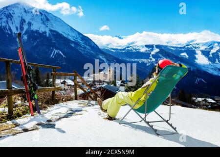 Une jeune femme se repose dans la chaise longue près de la paire de Ski observant les montagnes et les sommets alpins Banque D'Images