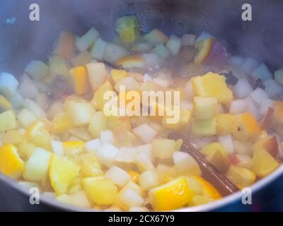 Ragoût de pommes et d'oranges finement hachées dans une casserole avec bâton de cannelle et épices Banque D'Images