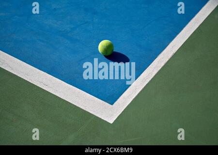 détail d'une balle de tennis jaune au coin de un terrain bleu avec des lignes blanches et un extérieur vert Banque D'Images