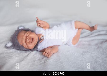 Mignon nouveau-né pleurs petit garçon dormant dans un lit de bébé dans un costume tricoté avec des oreilles. Modèle d'emballage pour bébés. Enfant en bonne santé, concept d'hôpital Banque D'Images