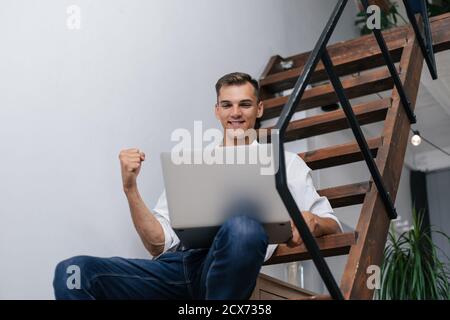 homme heureux avec un ordinateur portable assis sur les marches de son appartement. Banque D'Images
