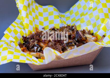 Poutine dans un papier-doublure jaune et blanc et un bac à papier. Les frites frites frites frites sont recouvertes de sauce foncée avec du fromage. Banque D'Images